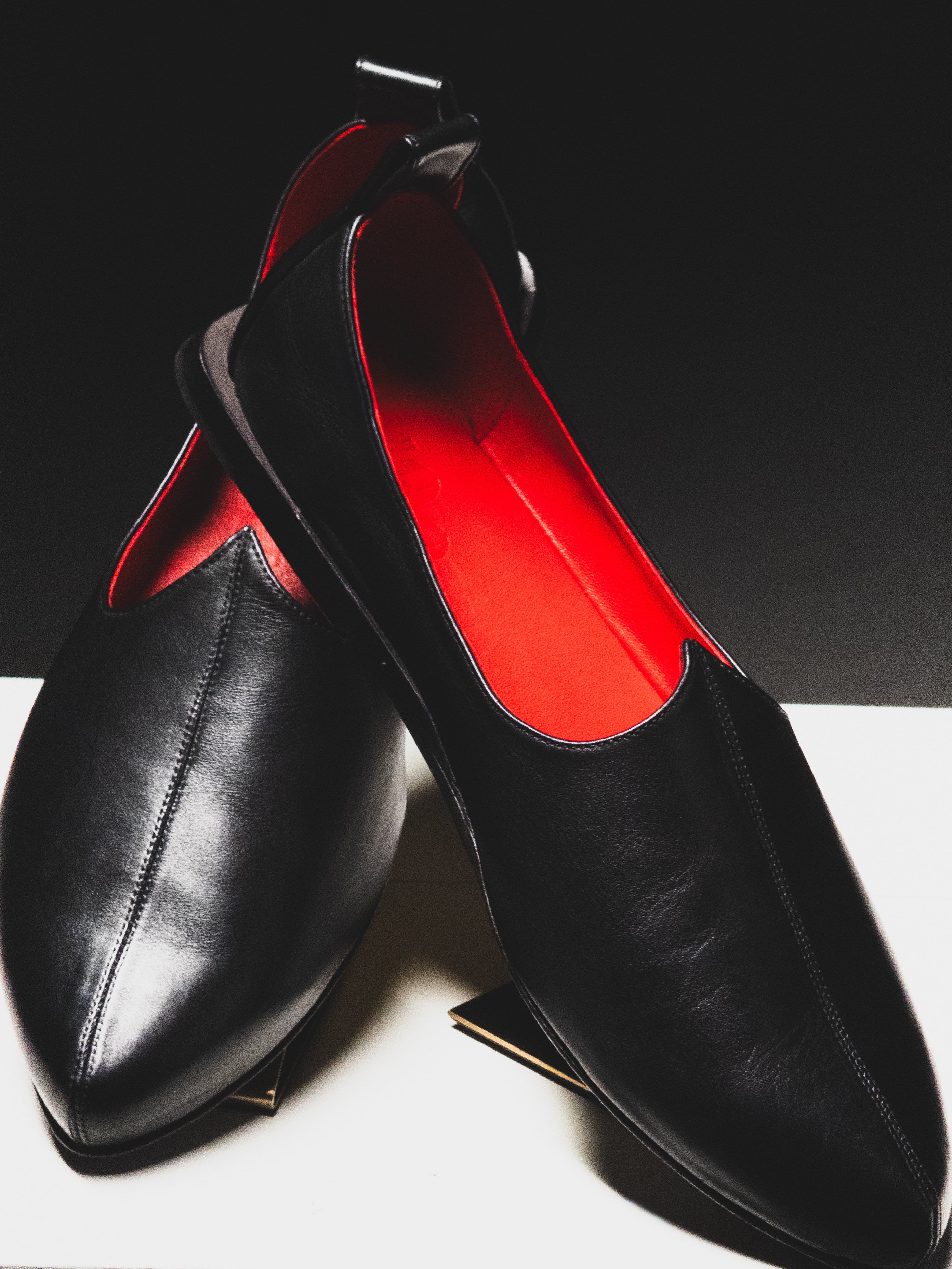 Handmade Black Rajasthani luxury Mojri with red lining on a white surface and black background