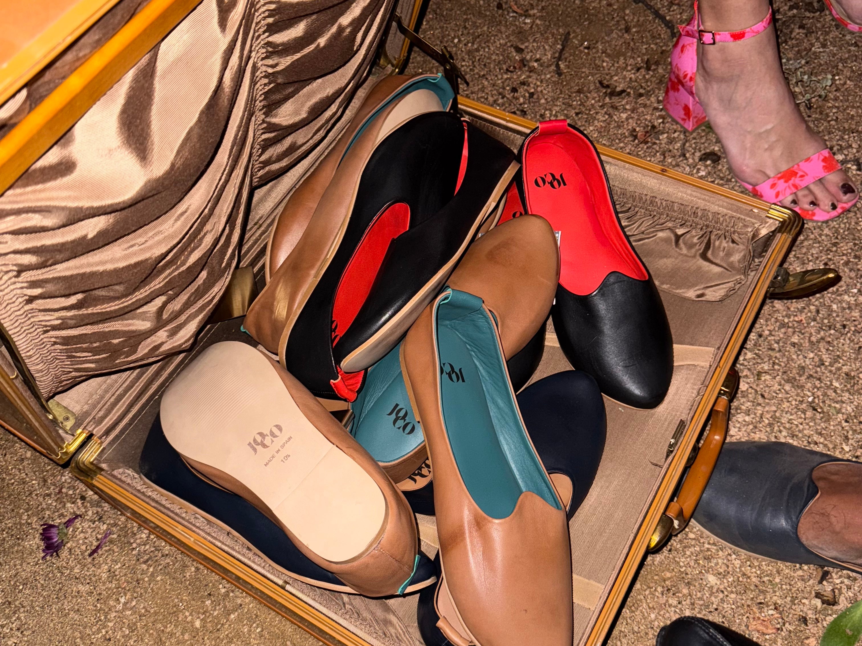 Open suitcase with various shoes on a concrete surface. JOCO shoes of color