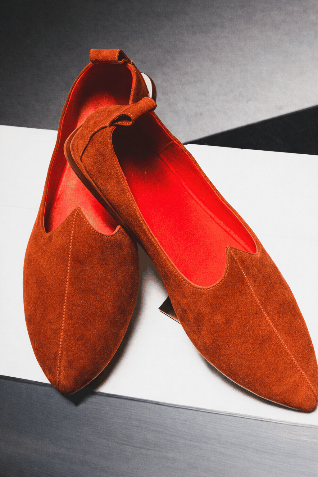 Brown suede shoes with red interior on a white surface. Handmade in Italy.