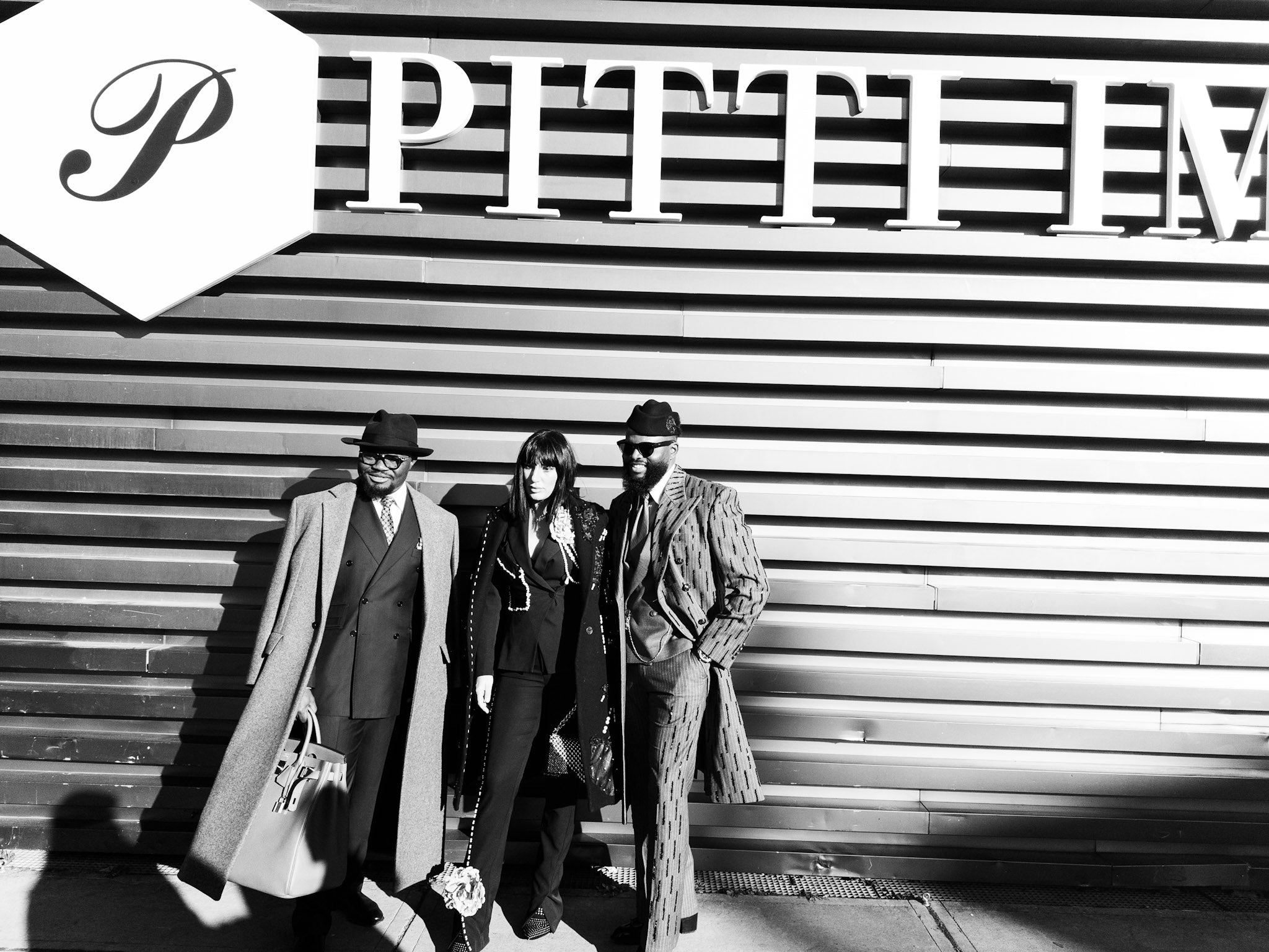 Three people standing in front of a striped wall with a large 'Pitti Uomo' logo. Photo by Udayan Joshi founder of JOCO