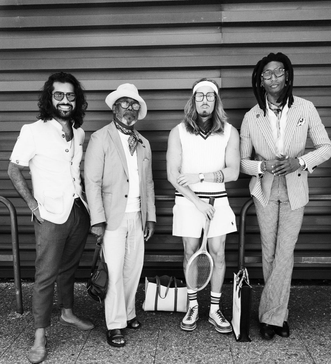 Black and white photo of four men posing outdoors, with one holding a tennis racket.