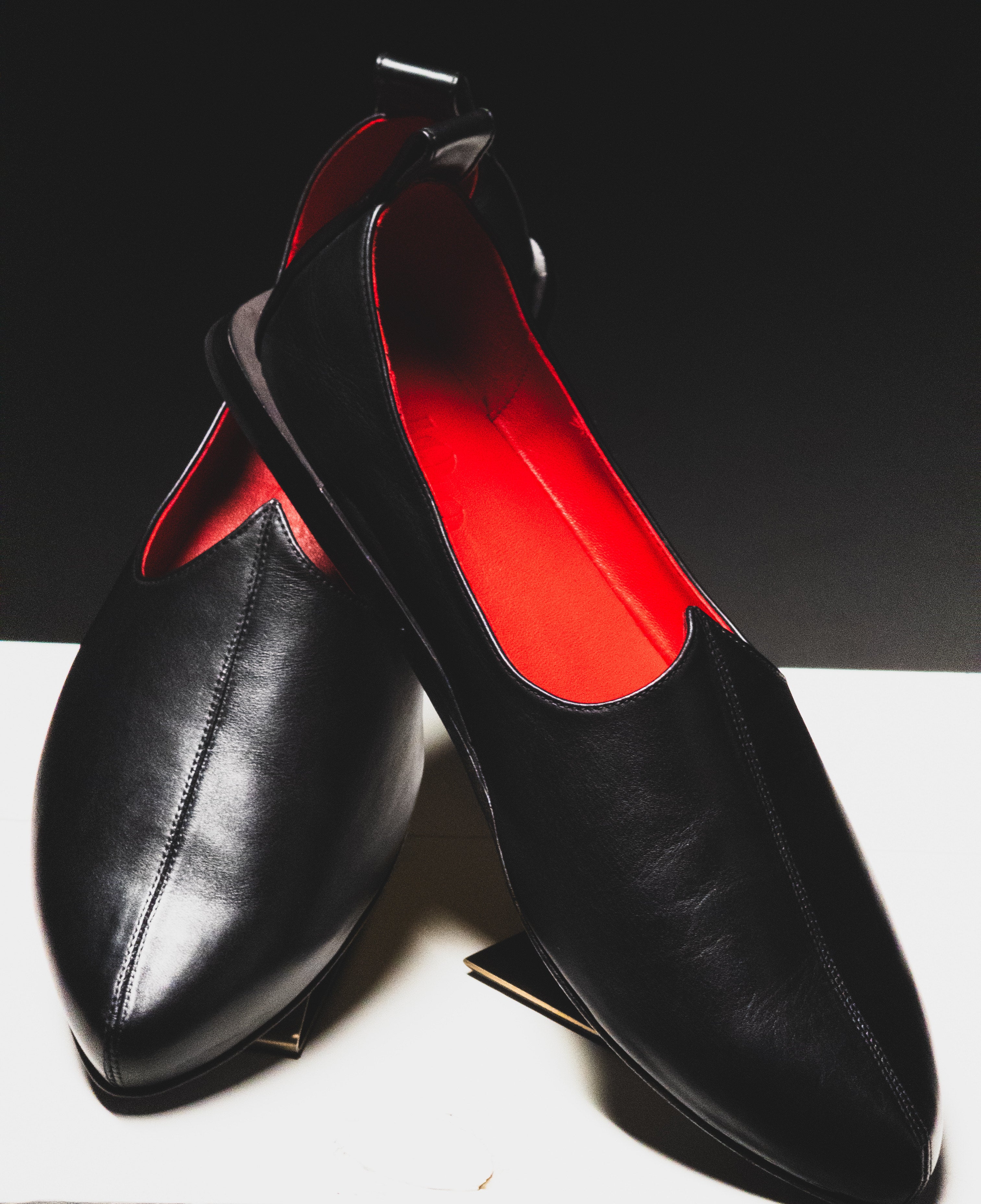 Handmade luxurious Black Rajasthani Mojri Loafers with red lining on a white surface and black background. 