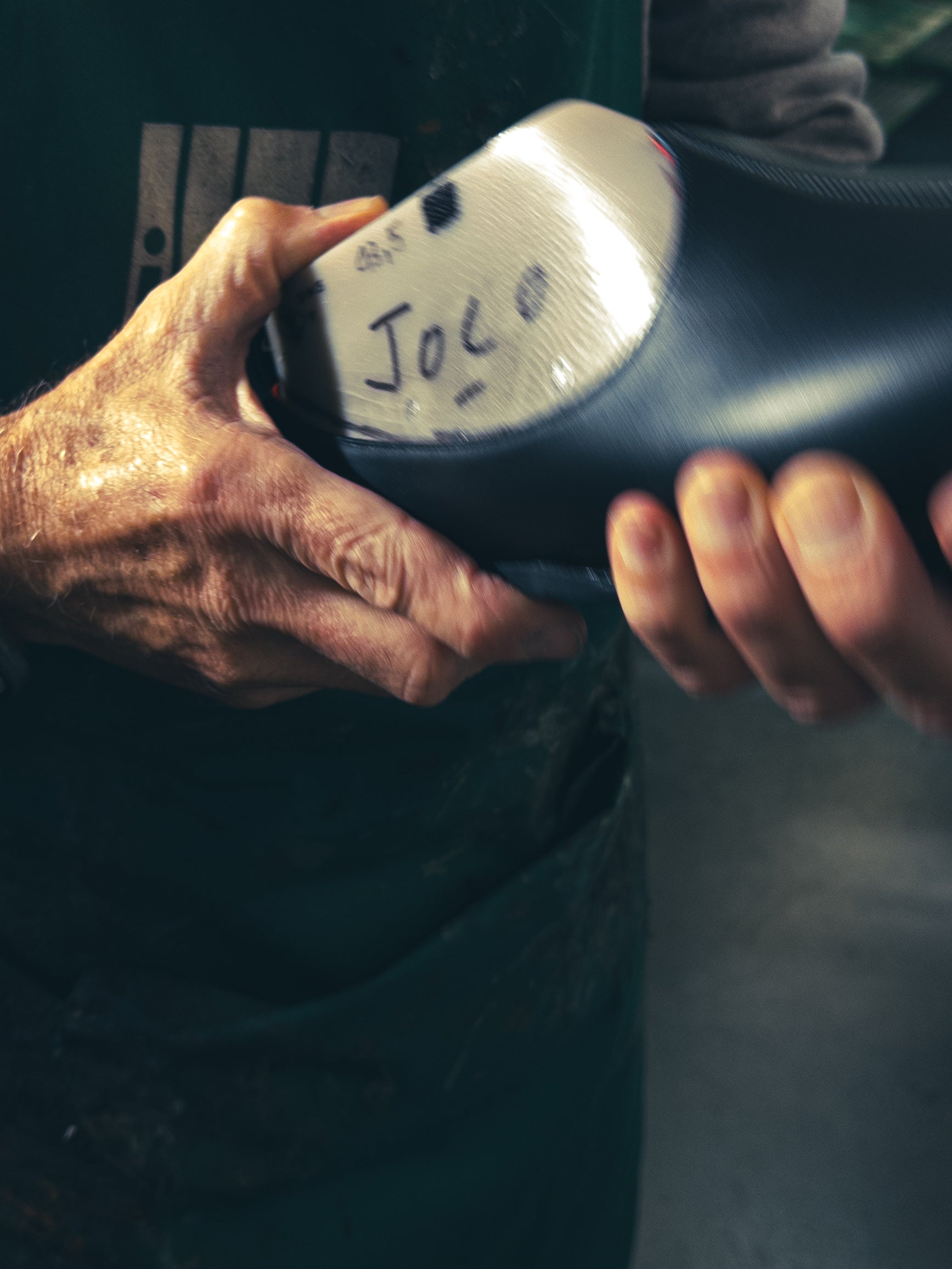 Close-up of a person's hands holding a shoe with 'Joco' written on it, against a blurred background. Handmade designer Italian loafers inspired by India